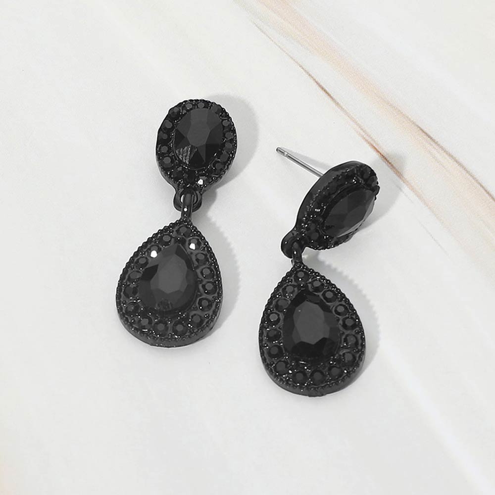 A pair of black-tone teardrop dangle earrings with black crystal center stones surrounded by smaller black rhinestones, displayed on a white marble surface.