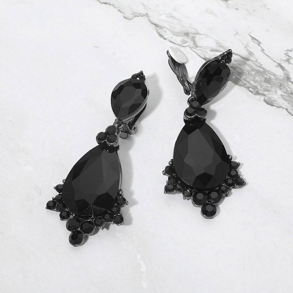 Jet black faceted teardrop clip-on statement earrings on black on a white marble background