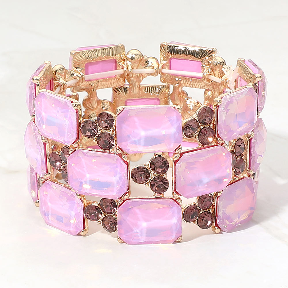A gold-tone stretch bracelet featuring rectangular lavender opal-like crystals and round darker purple faceted rhinestones, displayed on a light marble background.
