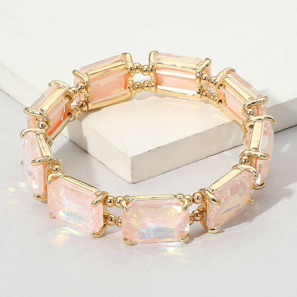 A gold-tone stretch bracelet featuring rectangular light pink emerald-cut crystals in a single row, displayed on a light background.