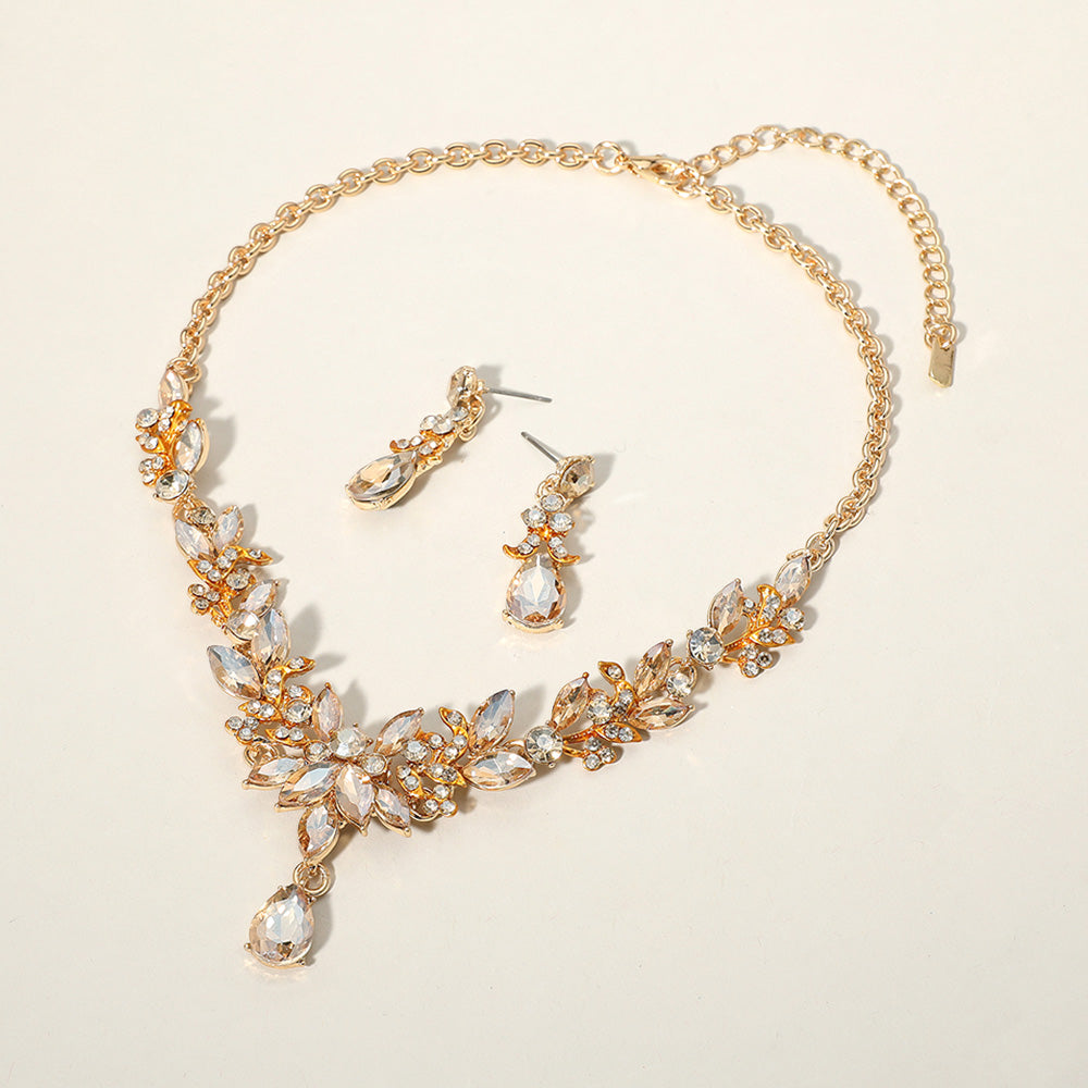 Light topaz gold stone crystal teardrop and marquise leaf necklace set on gold with matching earrings, elegant statement jewelry for bridal, prom, and evening wear on a beige background