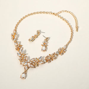 Light topaz gold stone crystal teardrop and marquise leaf necklace set on gold with matching earrings, elegant statement jewelry for bridal, prom, and evening wear on a beige background