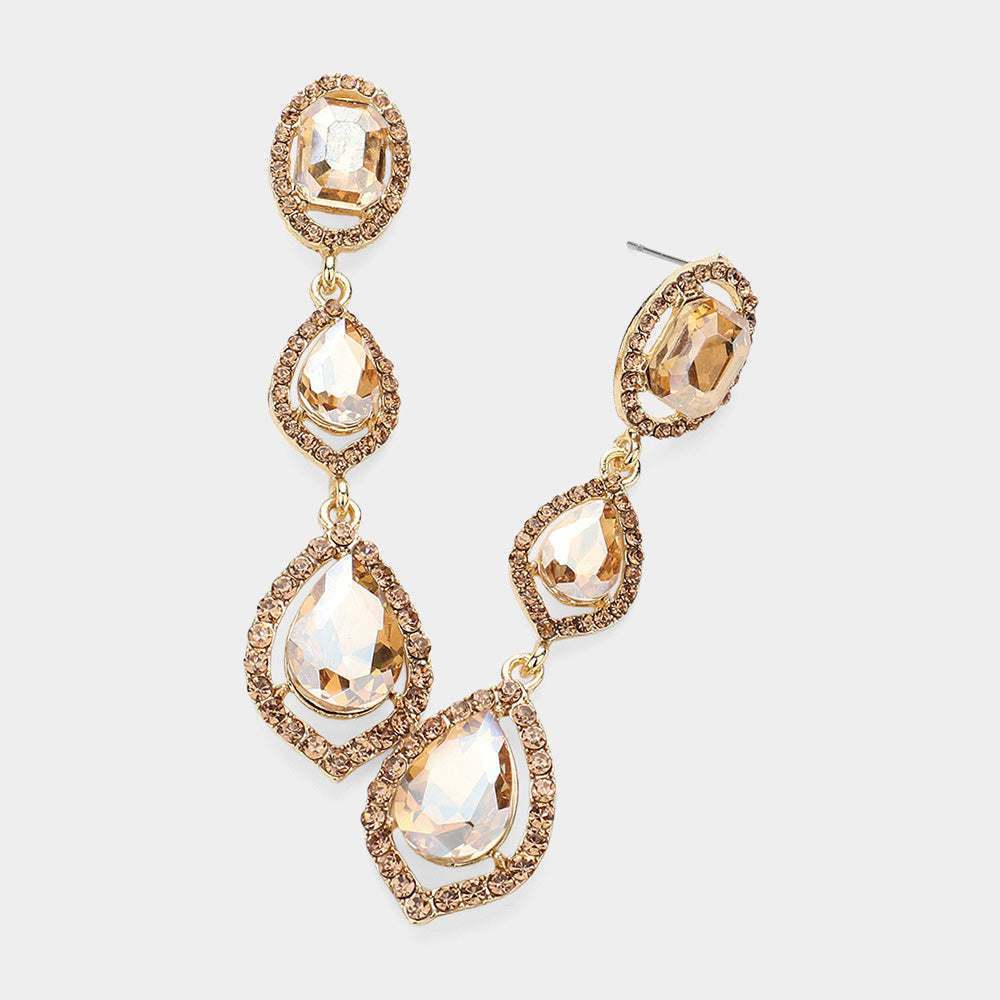 Pair of gold-tone drop earrings featuring large champagne gold oval and pear-shaped crystals surrounded by small clear stones on a light gray background.