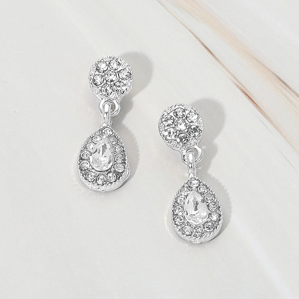 Little girls clear crystal teardrop halo earrings on silver displayed on a white marble background.