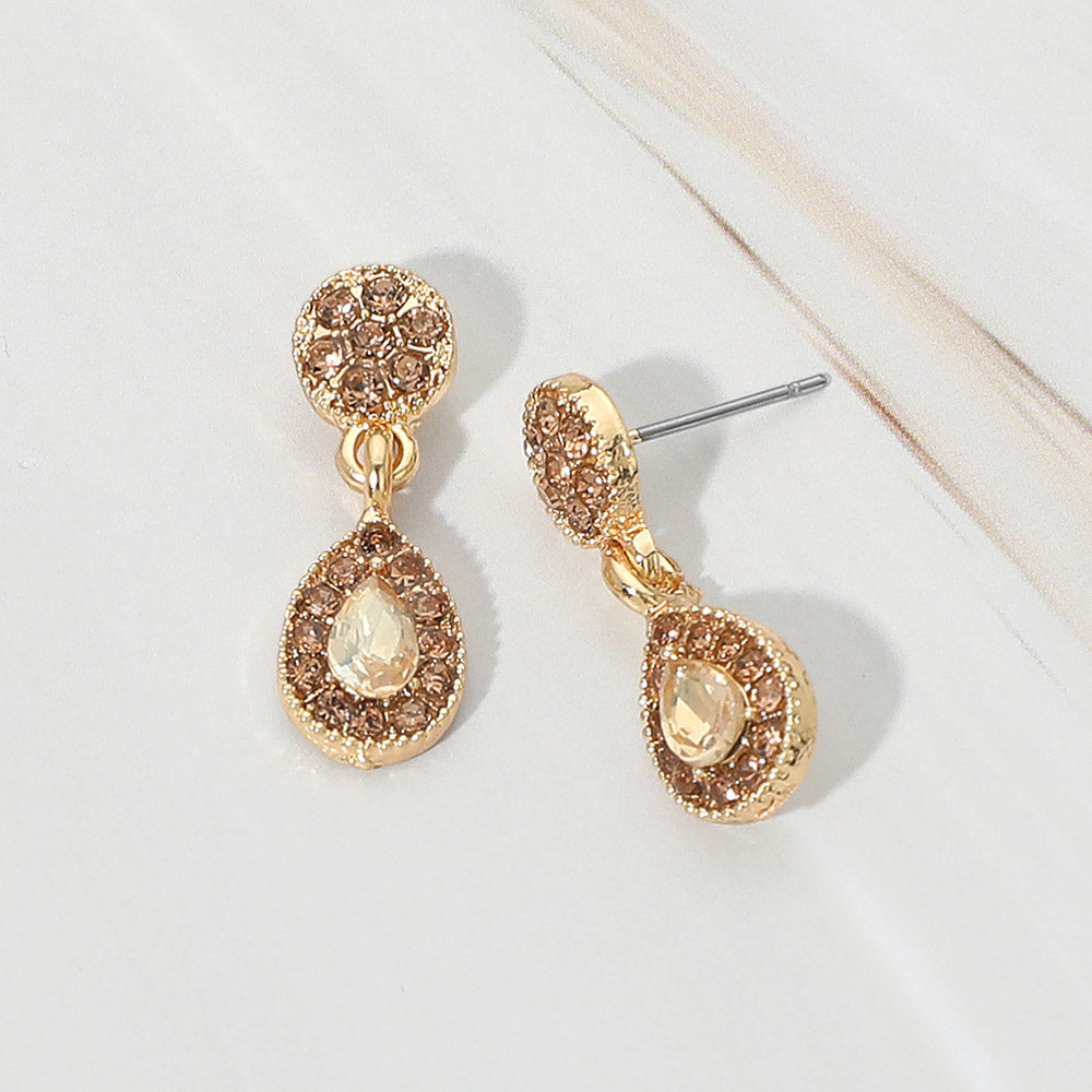 Little girls champagne gold stone crystal teardrop halo earrings on gold displayed on a white marble background.