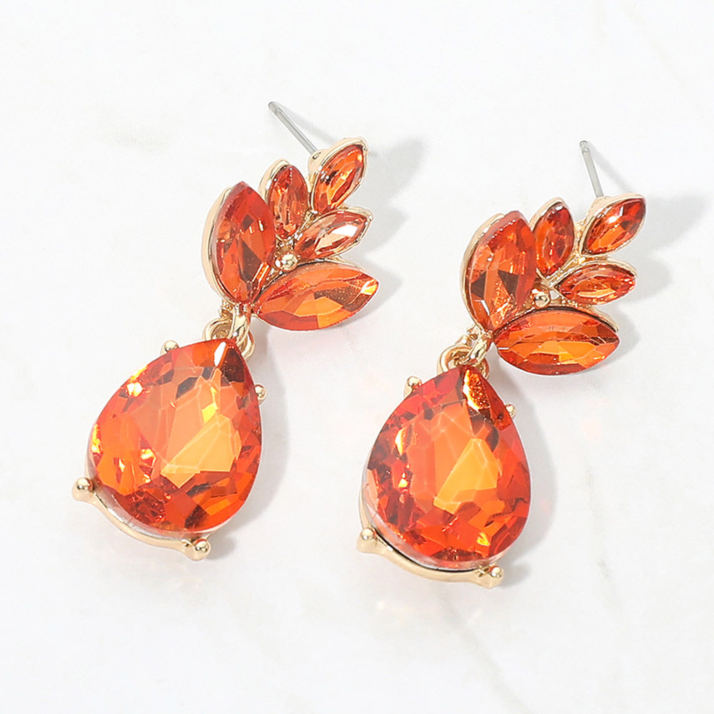 A pair of gold-tone drop earrings featuring faceted orange teardrop gemstones and smaller orange leaf-shaped stones, displayed on a clean white background.