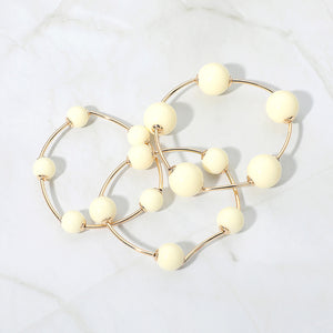 Ivory beaded stackable stretch bracelets on gold, shown here laid out individually on white marble background