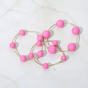 Pink beaded stackable stretch bracelets on gold, shown here laid out individually on white marble background