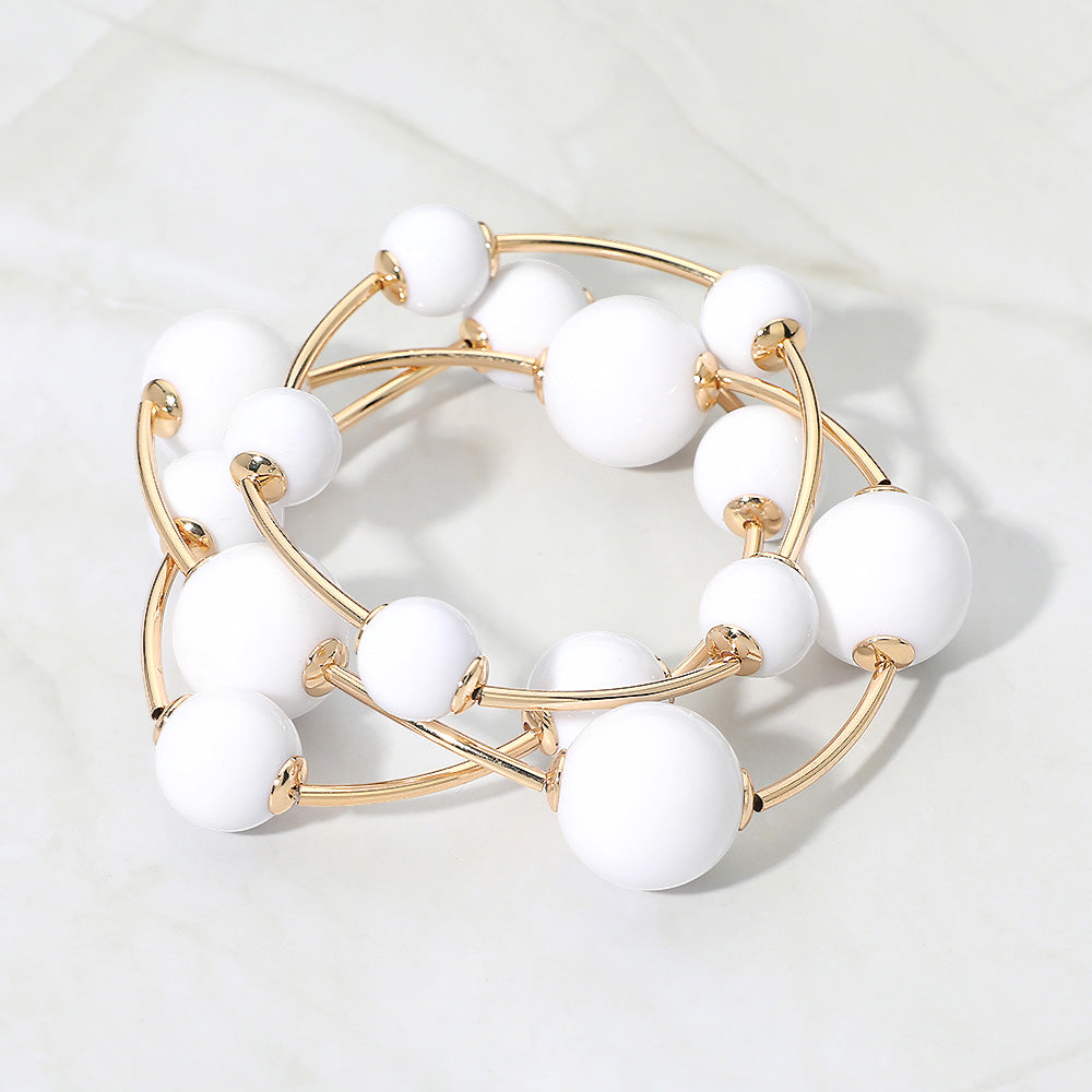 White beaded stackable stretch bracelets on gold on white marble background