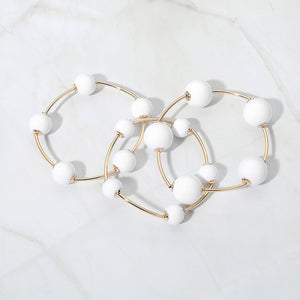White beaded stackable stretch bracelets on gold, shown here laid out individually on white marble background