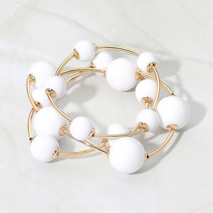 White beaded stackable stretch bracelets on gold on white marble background