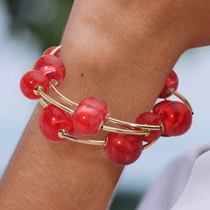 Close-up of a red chunky ball stretch bracelet set on a model’s wrist with a softly blurred background.