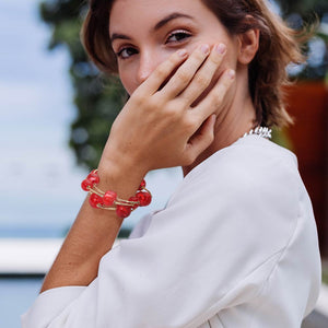 Woman wearing a red chunky ball 3-piece stretch bracelet set on gold with a softly blurred background.