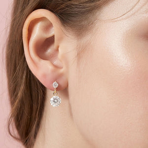 Little Girls' clear crystal round drop earrings on gold featuring a smaller round crystal suspended above a larger round crystal, displayed on a model's ear. 
