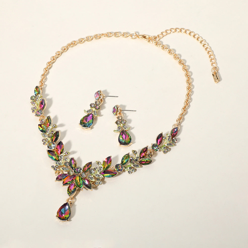 Multi-color crystal teardrop and marquise leaf necklace set on gold with matching earrings, bold statement jewelry for bridal, prom, and evening wear on a beige background