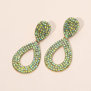 Green rhinestone pavé cut out teardrop pageant earrings on gold with brilliant crystal sparkle on beige background.