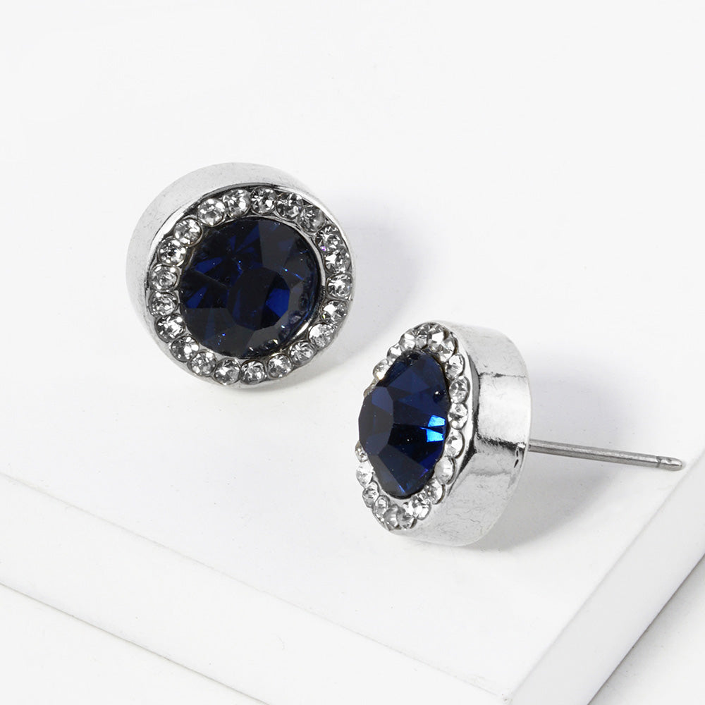 A pair of silver stud earrings with an oval navy blue faceted center stone surrounded by a halo of small clear rhinestones, displayed on a clean white surface.
