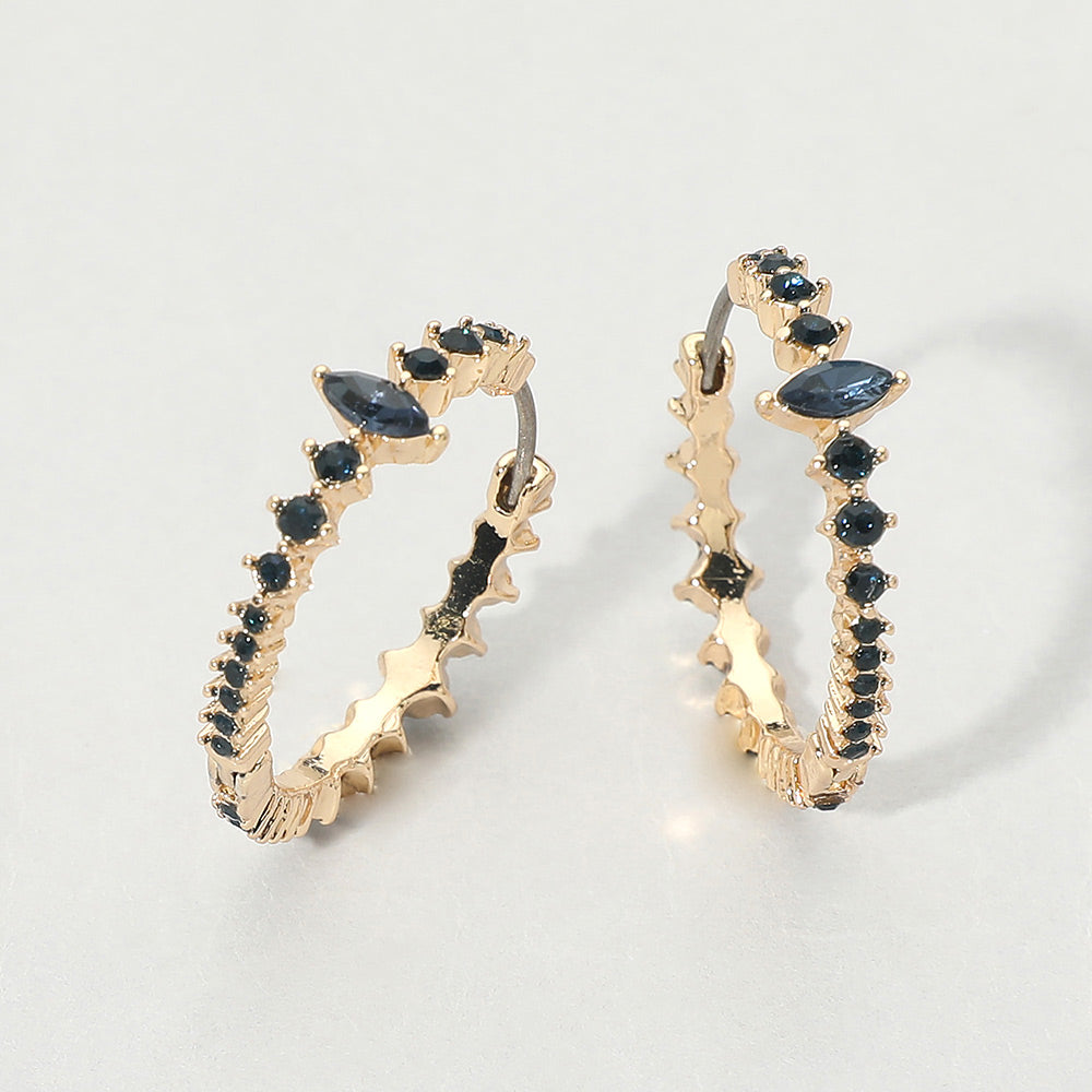 A pair of gold huggie hoop earrings with navy marquise and round gemstones, displayed on a light gray background.