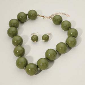 Olive Green chunky ball beaded statement necklace set with oversized round beads and matching drop earrings, displayed on a light cream background.