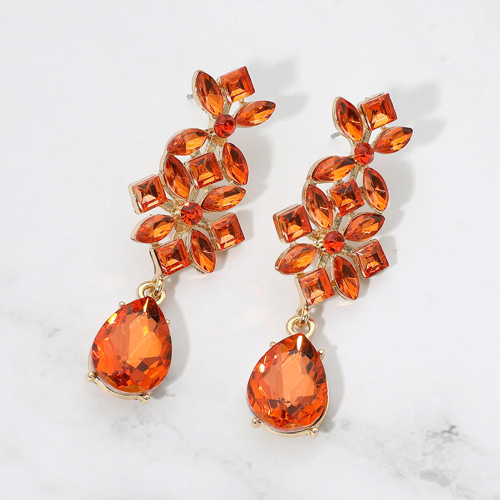 Orange crystal floral teardrop earrings on gold-tone metal, featuring clusters of marquise, square, and round stones above large faceted teardrop drops. Each earring measures approximately 0.8 inches wide by 2.5 inches long. Displayed on a white marble surface with gray veining.
