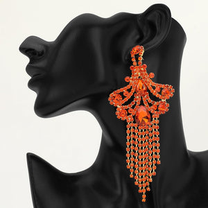 A large ornate Orange crystal statement earring on gold with cascading bead fringe and clear crystal accents on a black earring mannequin.