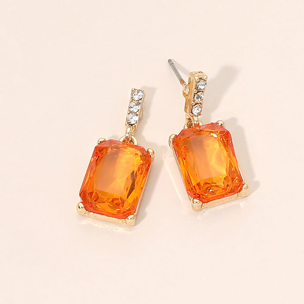 Gold-tone dangle earrings featuring large rectangular orange crystals with a short row of small clear crystals above each stone, displayed on a light beige background.