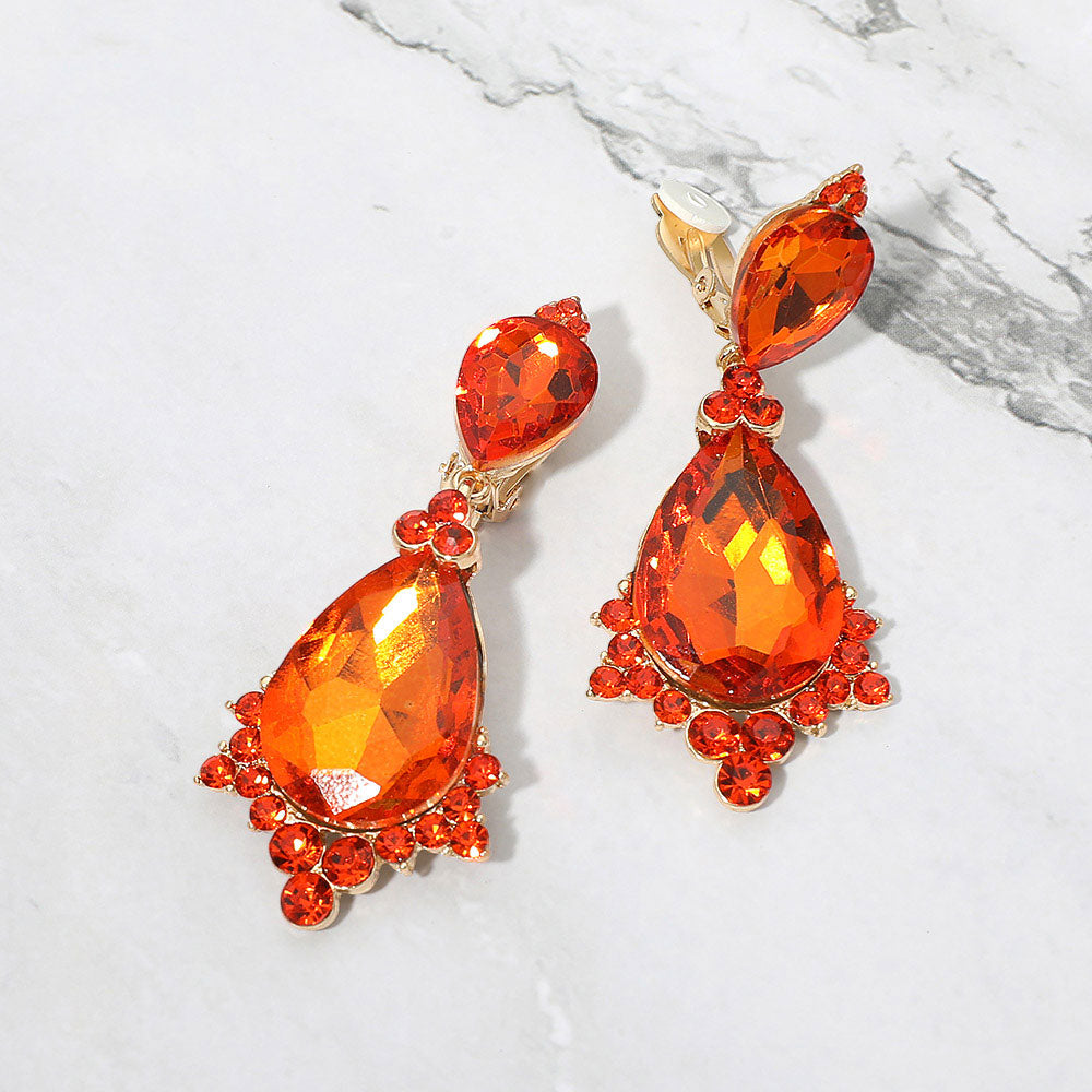 Orange faceted teardrop clip-on statement earrings on gold on a white marble background