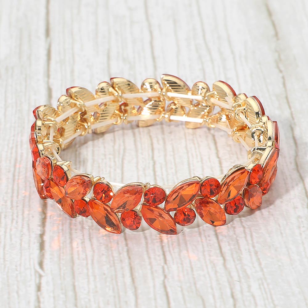 Orange marquise and round stone cluster stretch bracelet on gold on a light wood background