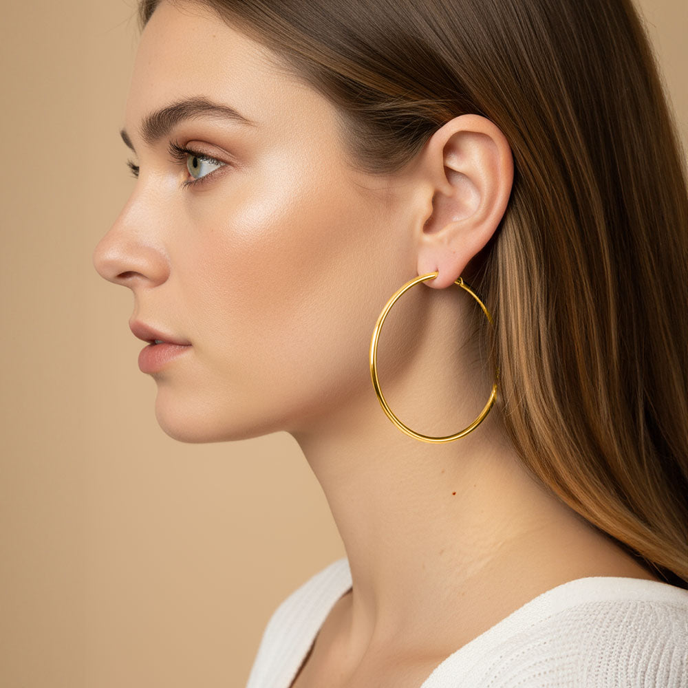 14K gold dipped hoop earrings in 2.4" size with pin catch on a pretty lady's ear, for pageants or casual wear. All is on a peach background.