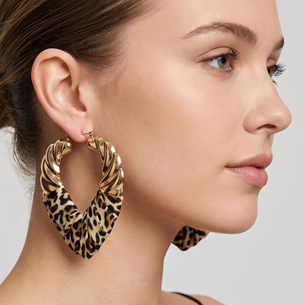A close-up side profile of a woman wearing large twisted hoop earrings with a leopard print pattern and gold-tone metal edges on a light gray background.