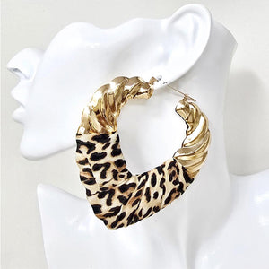 A large hoop earring displayed on a white mannequin head. The earring features a textured gold-tone twisted metal top and bottom, with a leopard-print fabric section in the middle.