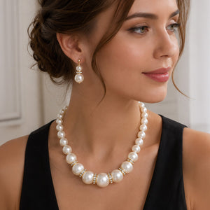 A woman wearing a cream oversized pearl and crystal statement necklace with graduated round pearls, clear crystal accents, and matching drop earrings.