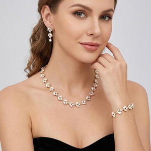 Cream pearl and crystal bridal jewelry set in a gold finish featuring a coordinating necklace, drop earrings, and bracelet with leaf-inspired accents, shown here on a model wearing the set.