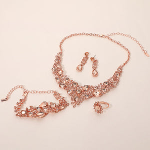 Peach crystal 4-piece jewelry set on rose gold with statement necklace, matching bracelet, drop earrings and adjustable ring arranged on a light beige background.