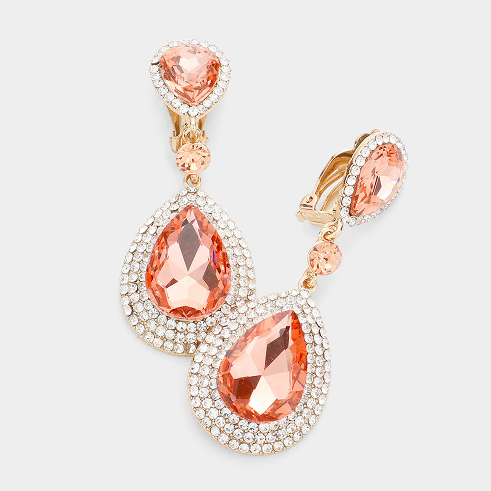 A pair of rose gold drop clip on earrings featuring large peach-colored teardrop gemstones surrounded by clear rhinestones, with smaller peach accent stones and heart-shaped peach gemstones at the top, shown on a light gray background.