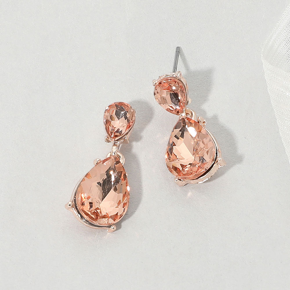 Double teardrop dangle earrings with peach crystals on rose gold, measuring 1 inch long by 0.4 inch wide, featuring smaller faceted teardrops above larger drops, displayed on a white textured surface.