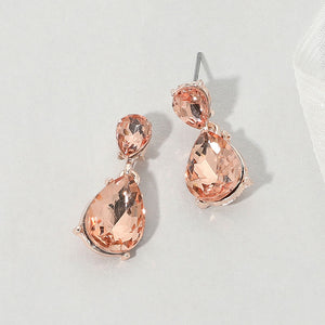 Double teardrop dangle earrings with peach crystals on rose gold, measuring 1 inch long by 0.4 inch wide, featuring smaller faceted teardrops above larger drops, displayed on a white textured surface.