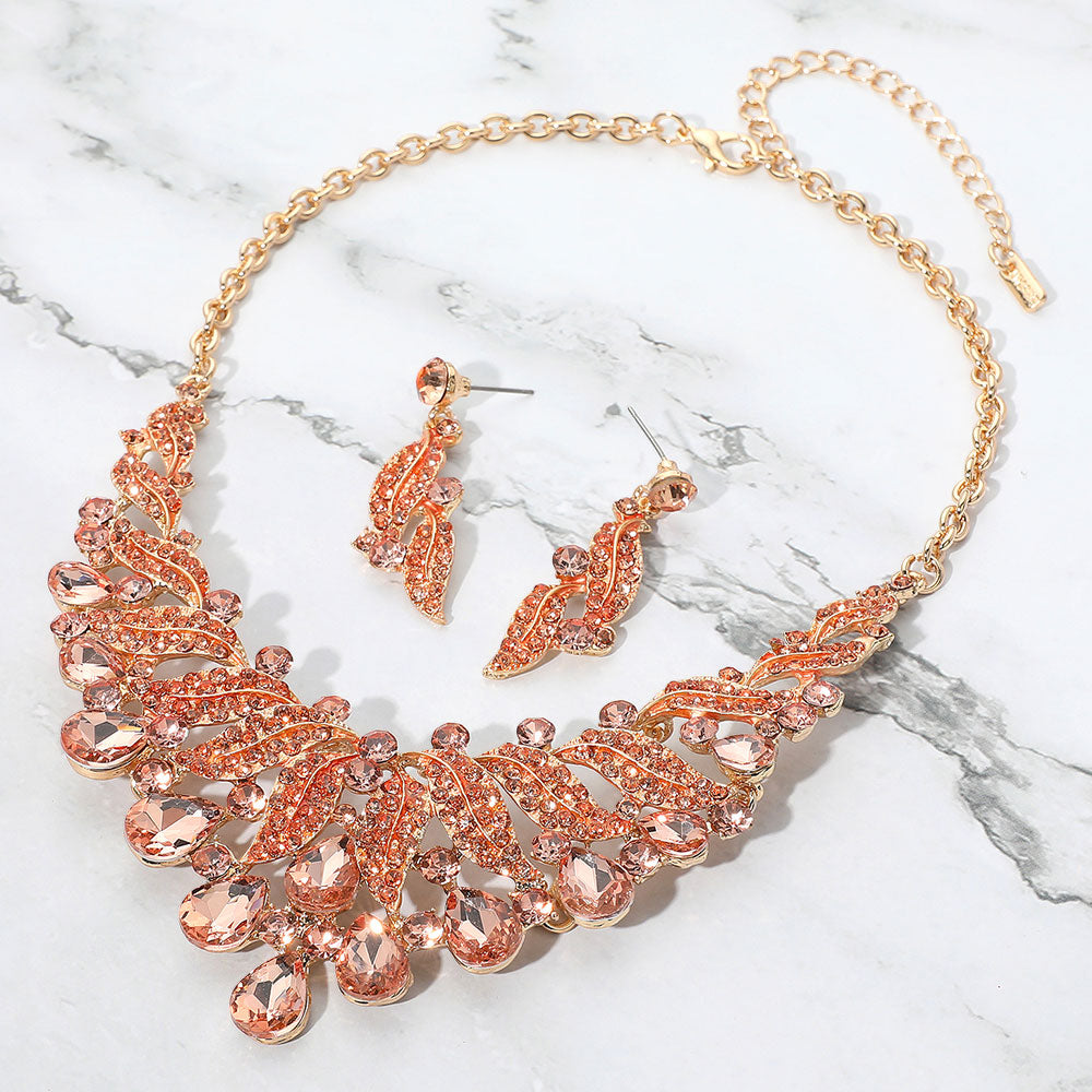Peach teardrop leaf crystal collar necklace set on gold with matching earrings, elegant statement jewelry for prom and evening wear on a marble background