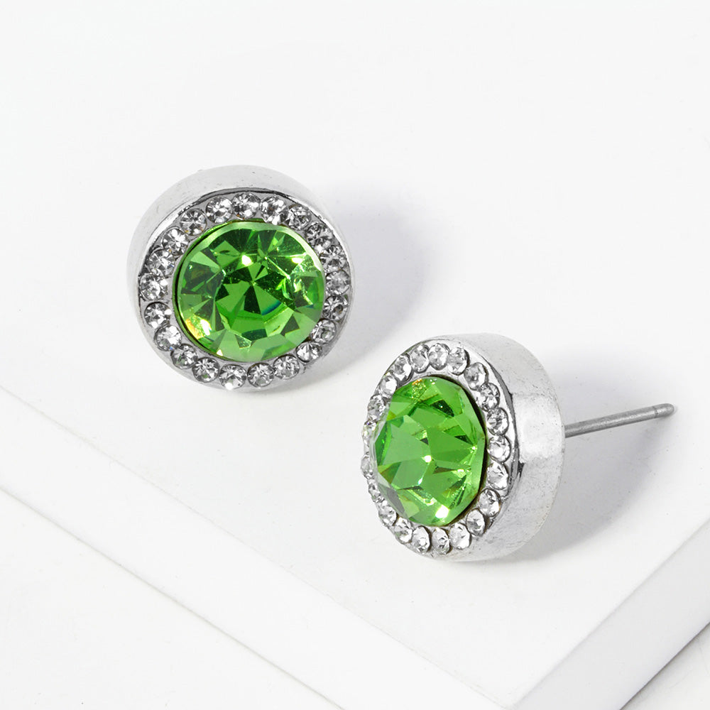 A pair of silver stud earrings with an oval peridot green faceted center stone surrounded by a halo of small clear rhinestones, displayed on a clean white surface.