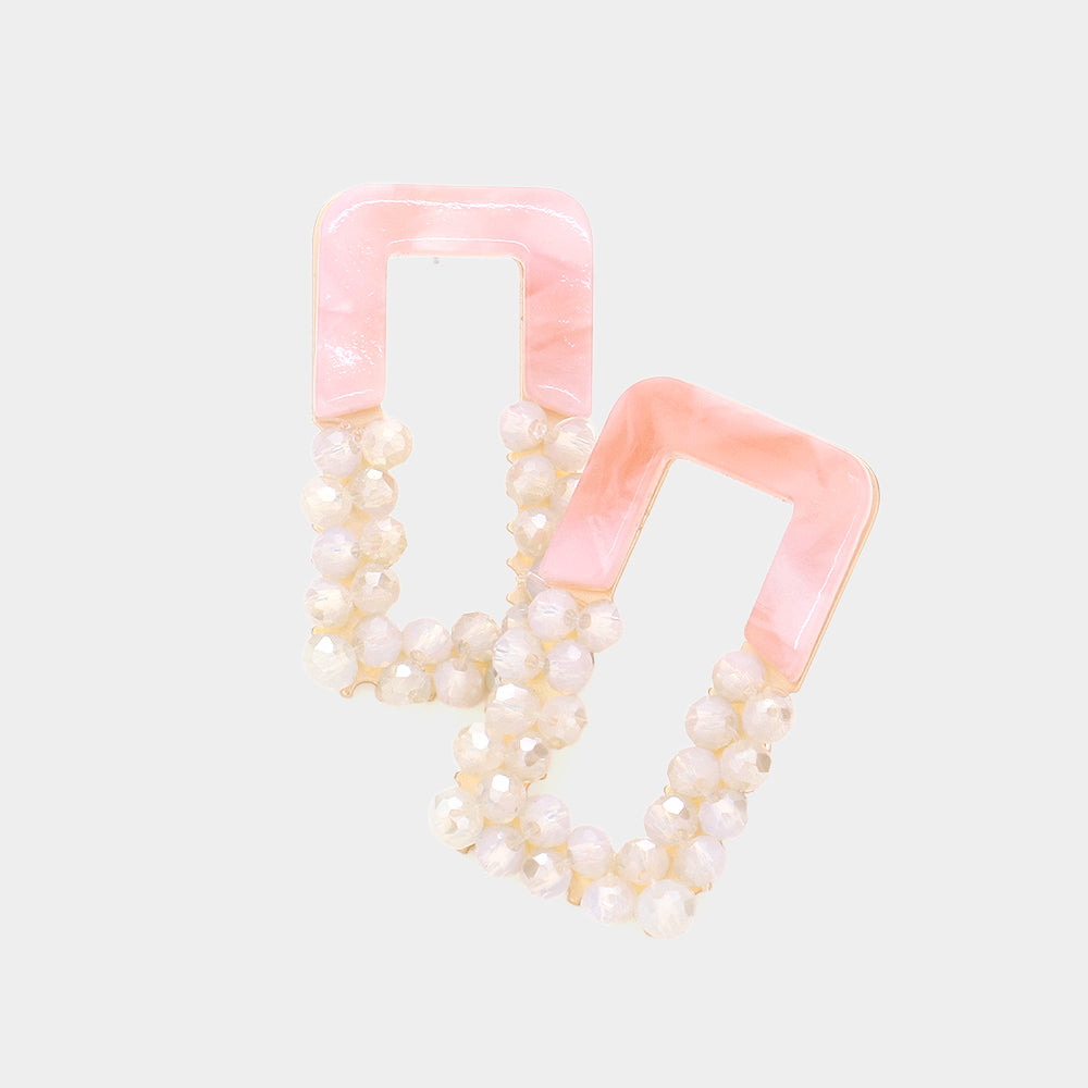 A pair of pink beaded open rectangle earrings with pearl-like bead accents, displayed on a light background.