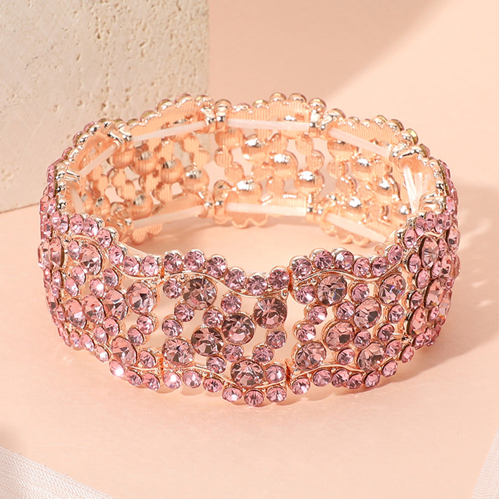 A wide, multi-strand stretch bracelet embellished with pink rhinestones and rose gold-toned metal, displayed on a soft peach background.