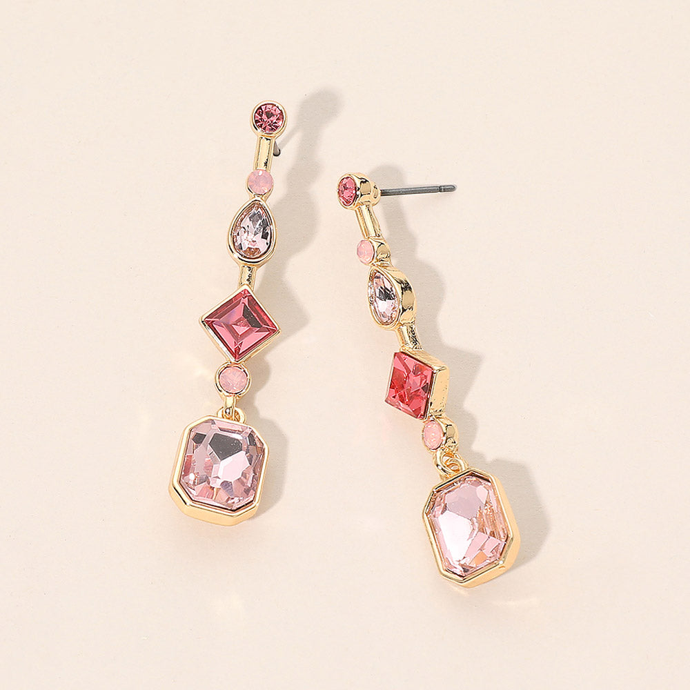A pair of gold-plated dangle geometric earrings featuring pink and clear faceted gemstones in various shapes, displayed on a light beige background.
