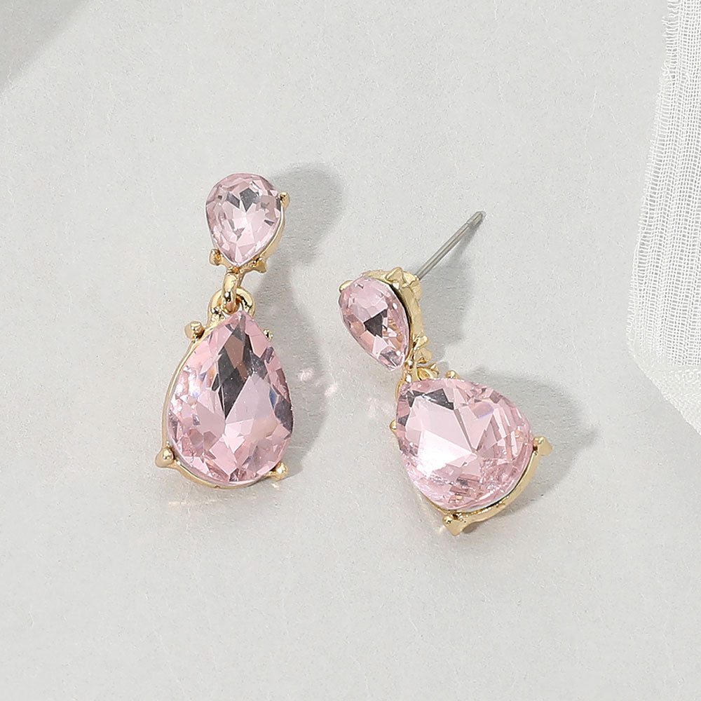 Double teardrop dangle earrings with pink crystals on gold, measuring 1 inch long by 0.4 inch wide, featuring smaller faceted teardrops above larger drops, displayed on a white textured surface.