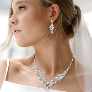 Clear teardrop rhinestone necklace set with V-shaped crystal design and matching earrings, all backed in silver, for prom and formal wear. Shown on a soft white background.