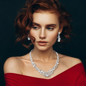 Clear teardrop rhinestone cluster necklace set on silver with matching earrings for prom and formal wear. Shown here on a woman on a black background.