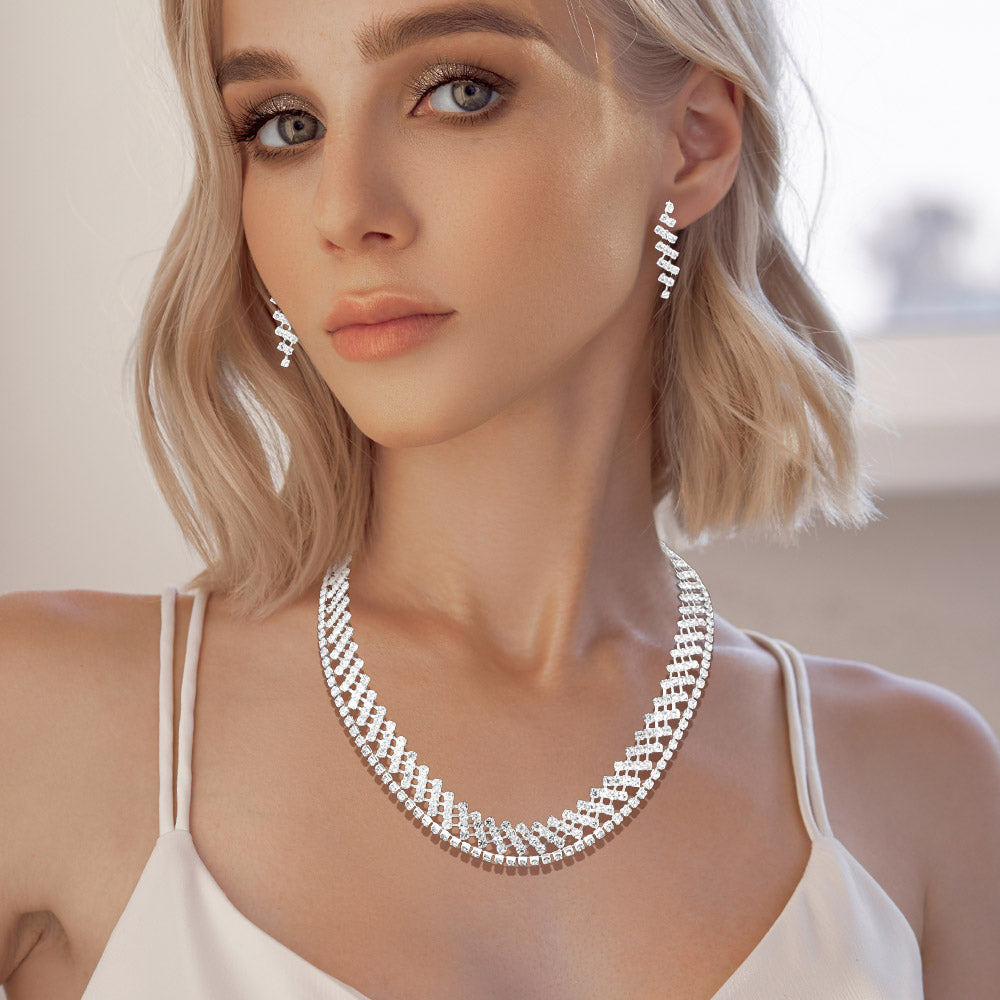 A woman wearing two separate clear crystal rhinestone necklaces layered together on silver with matching drop earrings against a light background.