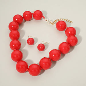 Red chunky ball beaded statement necklace set with oversized round beads and matching drop earrings, displayed on a light cream background.