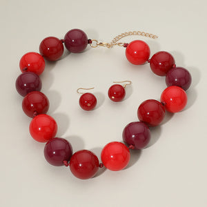 Red chunky ball beaded statement necklace set with oversized round beads and matching earrings, displayed on a beige background.
