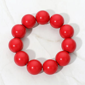 Red chunky ball beaded stretch bracelet with oversized round beads, displayed on a white marble background.