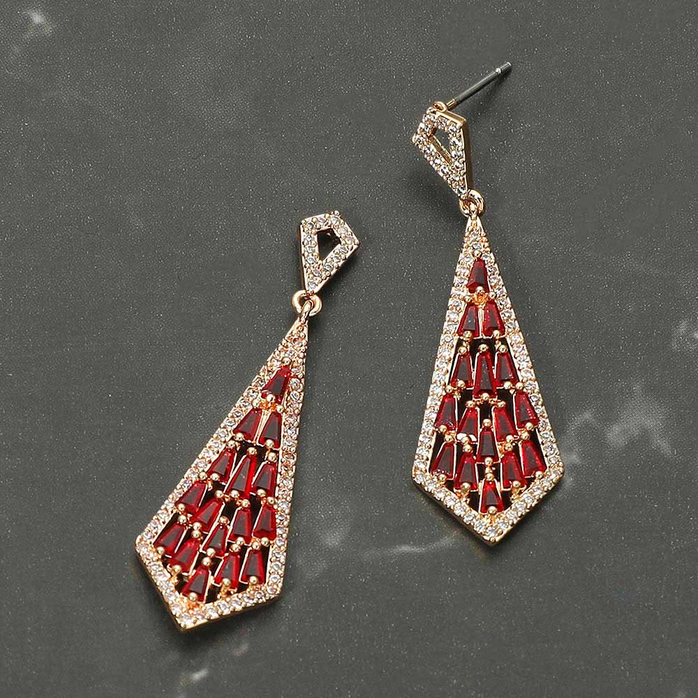 Red crystal geometric baguette drop earrings in a gold finish featuring baguette-cut red crystals arranged in an open geometric drop design, displayed on a grey stone background.